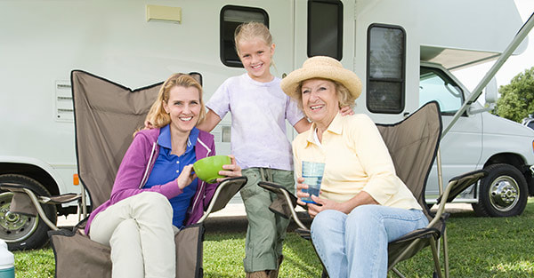 Grandmother and daughter sitting on a foldable chair  with standing granddaughter behind the RV car